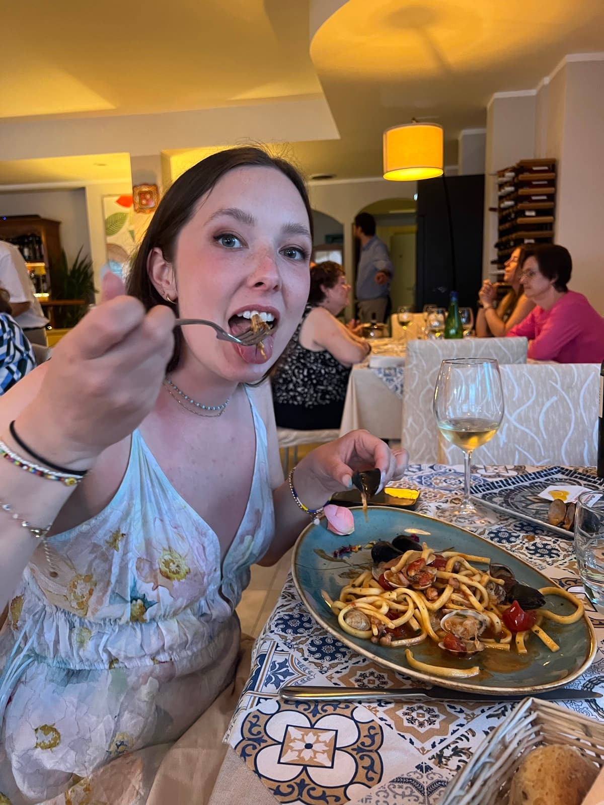 Taking a big forkful of pasta with clams and mussels at a restaurant, glass of white wine on the tiled table